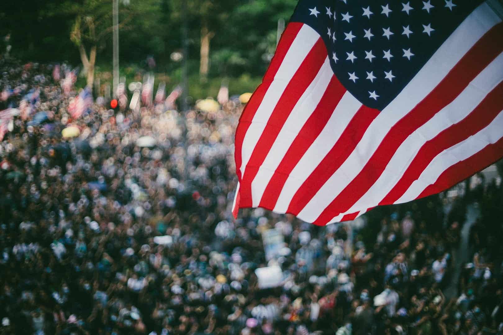 An American flag waving over a large crowd of people at an outdoor gathering.
