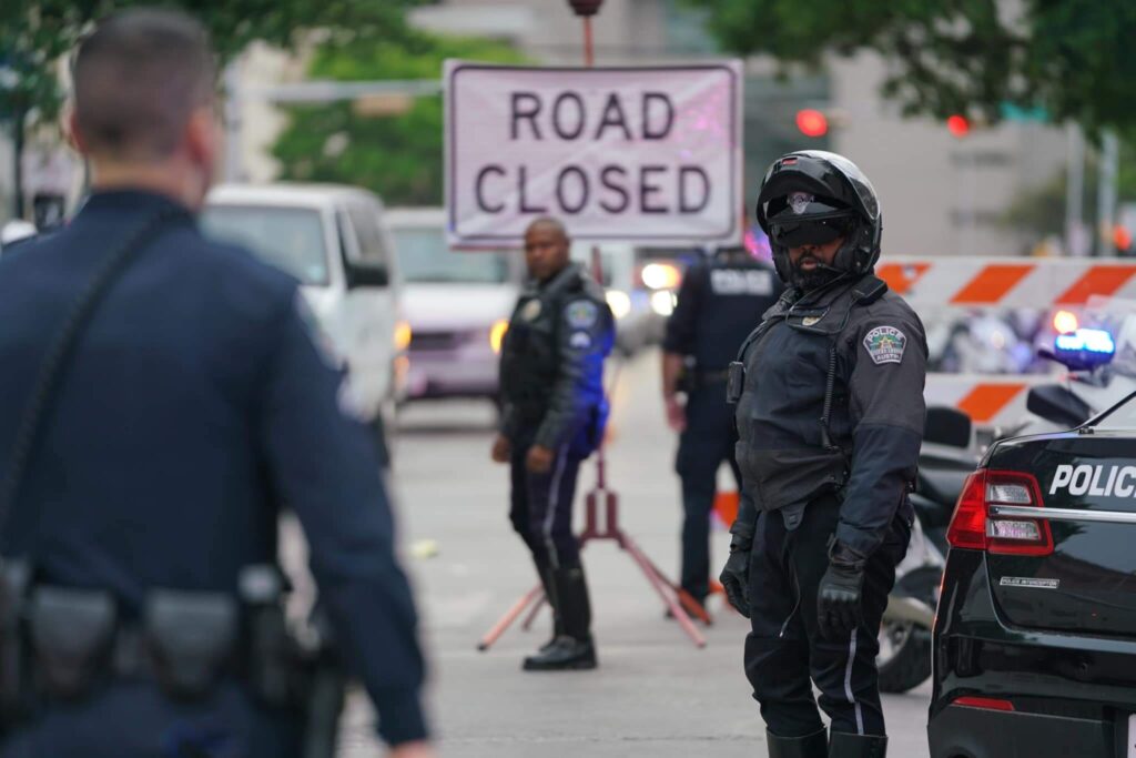 Police officers blocking a street with a "Road Closed" sign and barricades in the background.