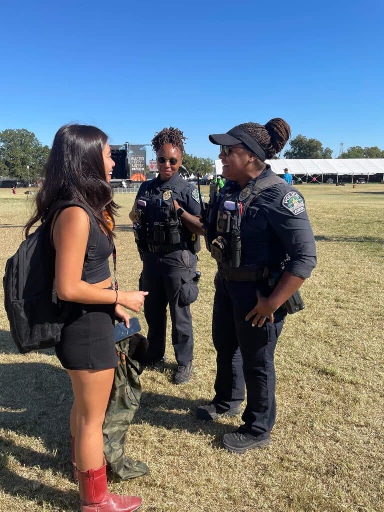A woman talking to two police officers in a grassy area with tents in the background.