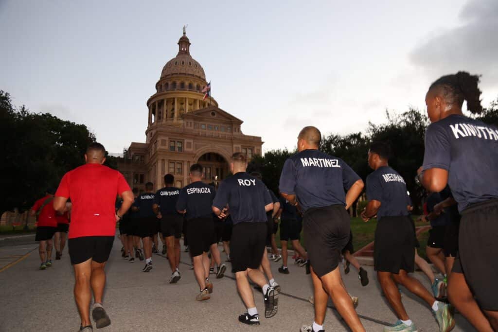 A group in athletic gear running past the Texas State Capitol building at dawn.