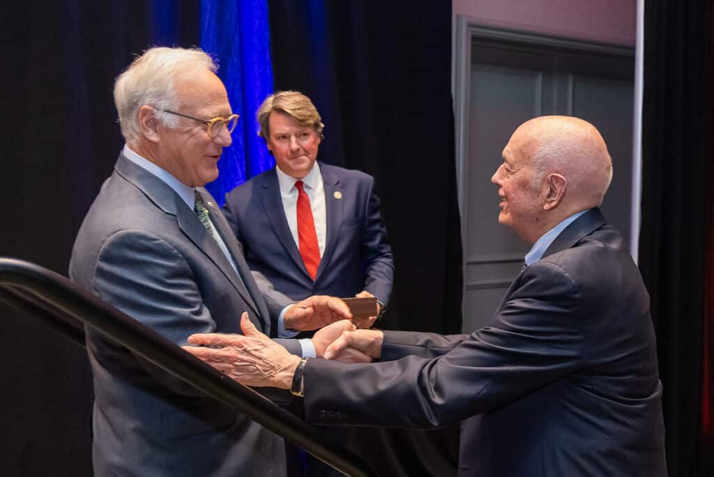 Three men in suits shaking hands at event.