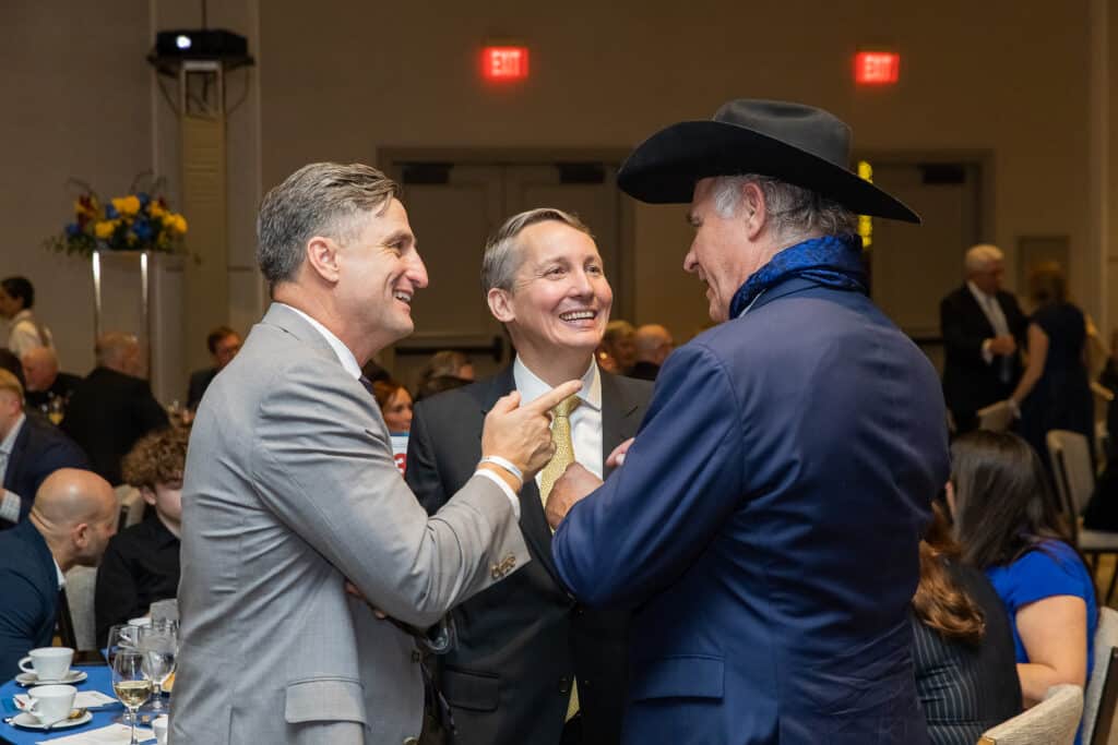 Three men talking and smiling at an event.