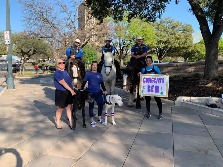 People with dogs and mounted police, holding congratulatory sign.