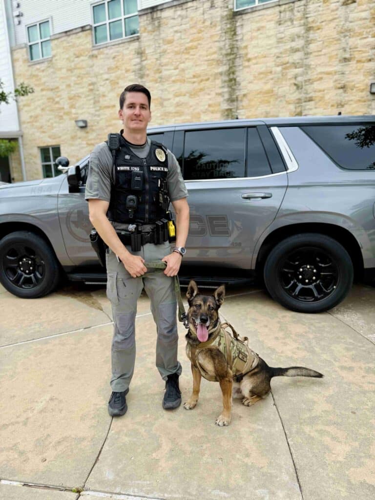 Police officer with K9 dog in front of vehicle.