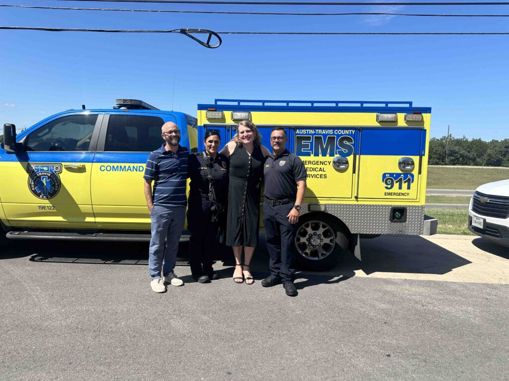 Four people smiling in front of EMS truck.