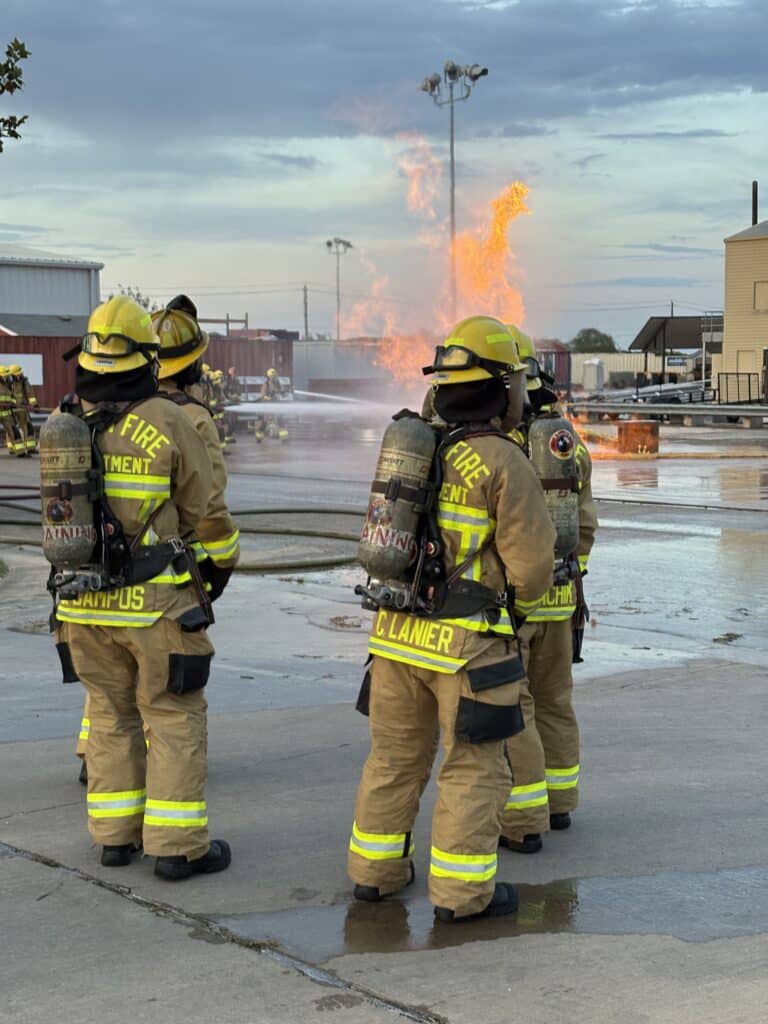 Firefighters observing live fire training exercise outdoors